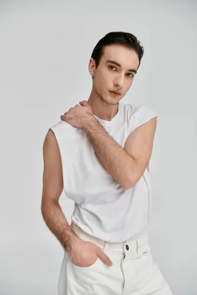 stock image A man in a white sleeveless shirt and white jeans poses confidently against a plain white backdrop.