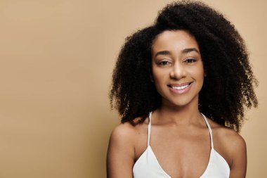 Doğal makyajlı güzel bir Afro-Amerikalı kadın bej bir arka plana gülümsüyor..