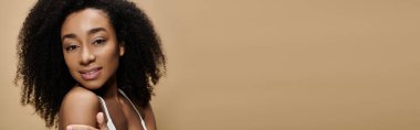Doğal makyajlı güzel bir Afro-Amerikalı kadın bej bir arka plana güvenerek gülümsüyor..
