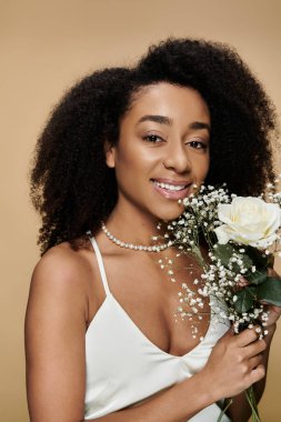 A beautiful African American woman with natural makeup holds a bouquet of flowers against a beige background. clipart