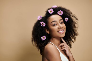 Güzel bir Afro-Amerikalı kadın, doğal makyajı ve saçlarında çiçeklerle bej bir arka plana gülümsüyor..