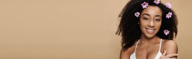 Güzel bir Afrikalı Amerikalı kadın parlak bir şekilde gülümser, doğal güzelliği saçlarındaki çiçeklerle güçlenir..