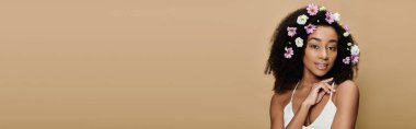 Güzel bir Afro-Amerikalı kadın, doğal makyajı ve saçlarında çiçeklerle bej bir arka plana gülümsüyor..