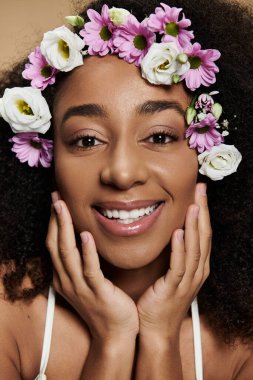 Saçları doğal makyajlı ve çiçekli güzel bir Afro-Amerikalı kadın bej bir arka plana doğru gülümsüyor..