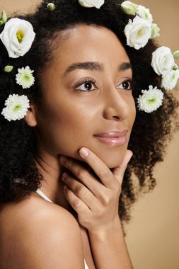 Doğal makyajlı ve saçında çiçekler olan güzel bir Afro-Amerikalı kadın bej arka planda poz veriyor..