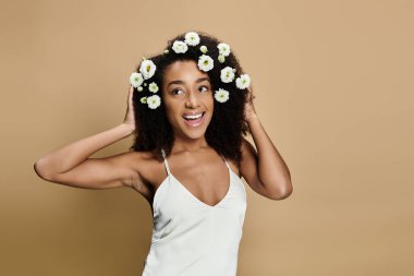 Saçları doğal makyajlı ve çiçekli güzel bir Afro-Amerikalı kadın bej bir arka plana doğru gülümsüyor..