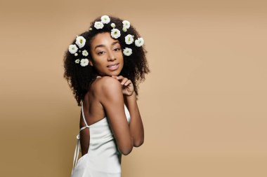 A beautiful African American woman with natural makeup and flowers in her hair poses against a beige background. clipart