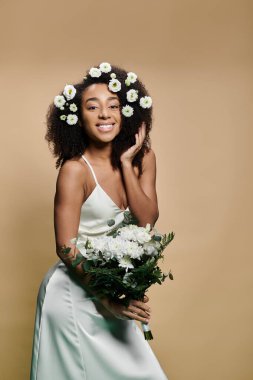 Beyaz elbiseli güzel bir Afro-Amerikalı kadın, saçına çiçekler takmış, elinde buket tutarken kameraya gülümsüyor..