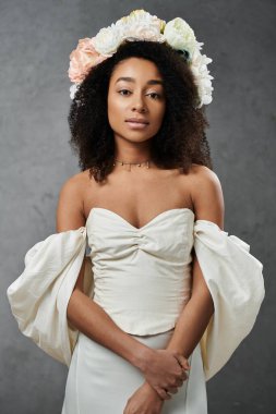 A stunning African American bride poses in a white wedding dress with flowers in her hair against a grey background. clipart