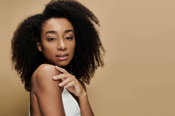 A beautiful African American woman with natural makeup poses against a beige background.