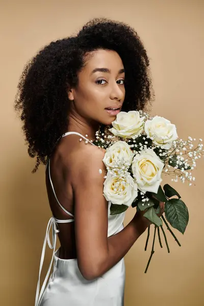 stock image An African American woman in a white dress holds a bouquet of white roses against a beige background.