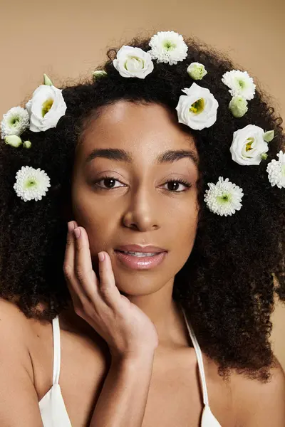 stock image A beautiful African American woman with natural makeup and flowers in her hair poses against a beige background.