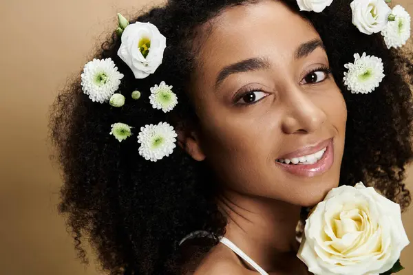 stock image A beautiful African American woman with natural makeup smiles warmly with flowers adorning her hair against a beige background.