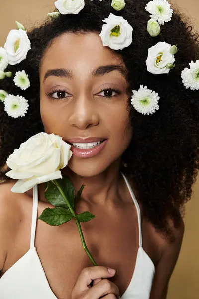 stock image A beautiful African American woman with natural makeup smiles softly while holding a white rose and wearing a flower crown.