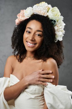 Güzel bir Afro-Amerikan gelini çiçek tacıyla ışıl ışıl gülümsüyor, beyaz elbisesi ve çiçek aksanı çarpıcı bir görüntü oluşturuyor..