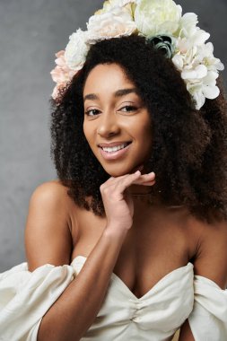 A beautiful African American bride wearing a white wedding dress and a floral crown smiles radiantly against a grey backdrop. clipart