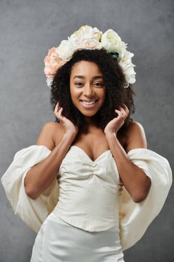 Beyaz gelinlik içinde güzel bir Afro-Amerikalı gelin çiçekli taç giyerken gülümsüyor..