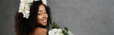Beyaz bir gelinlik giymiş güzel bir Afro-Amerikan gelini ve çiçekli taç gri bir arka plana gülümsüyor..