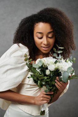 Beyaz bir gelinlik giymiş güzel bir Afrikalı Amerikalı gelin elinde bir buket beyaz çiçek tutuyor..