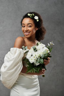 Beyaz gelinlik içinde güzel bir Afro-Amerikalı gelin elinde bir buket beyaz çiçek tutuyor..