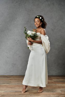 Güzel bir Afrikalı Amerikalı gelin beyaz bir gelinlik içinde saçlarında çiçeklerle poz veriyor..