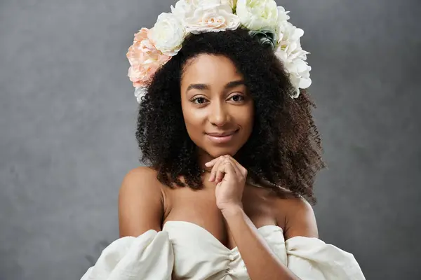 stock image A beautiful African American bride poses in a white wedding dress with flowers in her hair against a grey background.