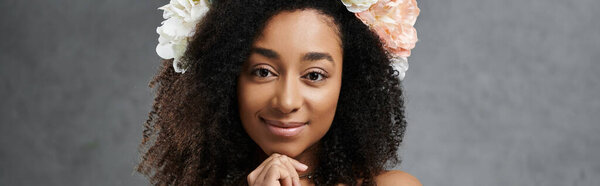 A beautiful African American bride in a white wedding dress, with flowers in her hair, smiles sweetly against a grey background.