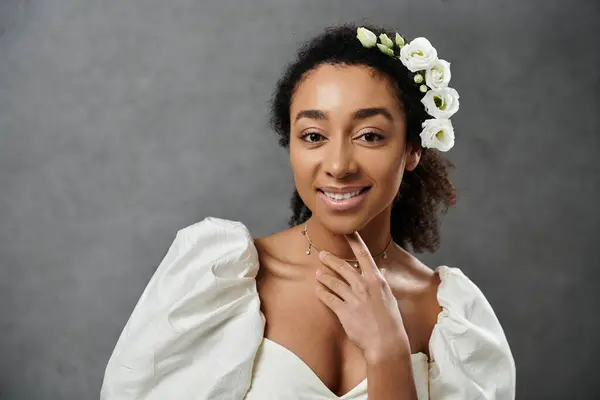 stock image A beautiful African American bride in a white wedding dress with flowers in her hair smiles against a grey background.