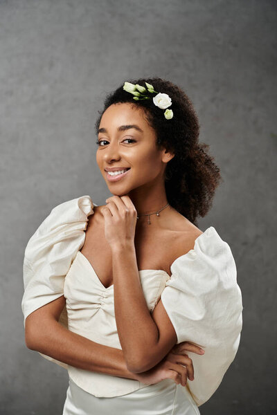 A beautiful African American bride in a white wedding dress with flowers in her hair smiles radiantly against a grey backdrop.
