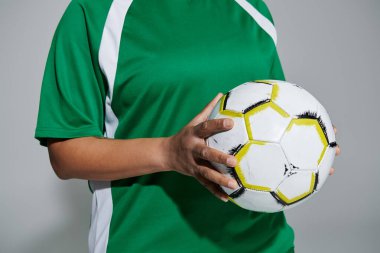 Yeşil beyaz formalı bir kadın elinde bir futbol topu tutuyor..