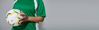 Yeşil formalı bir kadın elinde futbol topu tutuyor, oynamaya hazır..