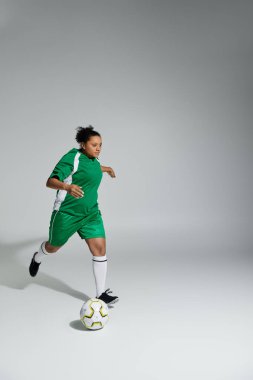 Yeşil futbol forması giyen bir kadın stüdyo ortamında top sürüyor..