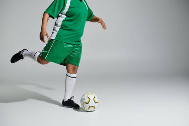 Yeşil futbol formalı bir kadın sağ ayağıyla top sürüyor..