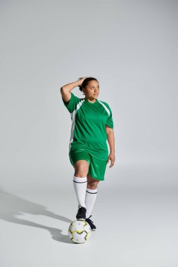 Beyaz arka planda yeşil formalı kendine güvenen bayan sporcu, futbol topunda ayak.