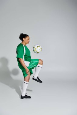 Yeşil futbol formalı bir kadın stüdyo ortamında futbol topuyla hokkabazlık yapıyor..