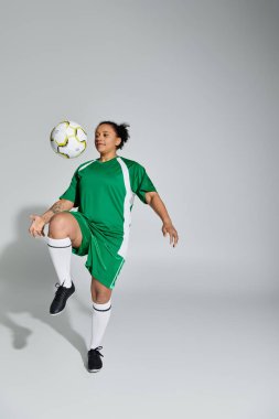Yeşil futbol formalı bir kadın stüdyo ortamında futbol topuyla hokkabazlık yapıyor..