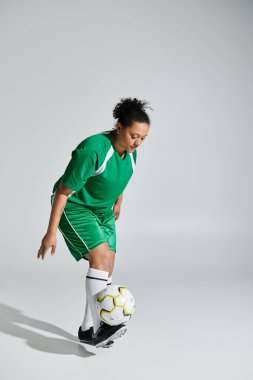 Yeşil formalı bir bayan futbolcu stüdyo ortamında futbol topuyla hokkabazlık yapıyor..