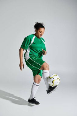 Yeşil futbol formalı bir kadın stüdyo ortamında futbol topuyla hokkabazlık yapıyor..