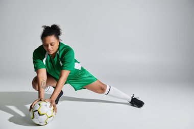 Yeşil forma giyen bir bayan atlet, elinde futbol topuyla beyaz arka planda esniyor..