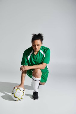 Yeşil formalı bir bayan sporcu önünde bir futbol topuyla diz çöker..