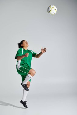 Yeşil üniformalı bir bayan atlet futbol maçında topun başına atlıyor..