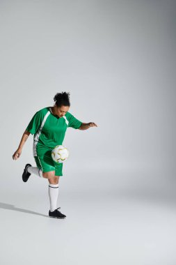 Yeşil futbol formalı bir kadın, beyaz bir stüdyonun arka planında dururken topla hokkabazlık yapıyor..