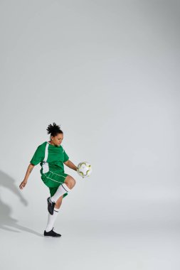 Yeşil futbol formalı bir kadın stüdyo ortamında beyaz bir topla hokkabazlık yapıyor..