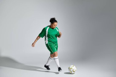 Yeşil futbol formalı bir bayan atlet stüdyo ortamında top sürüyor..
