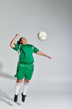 Yeşil futbol formalı bir bayan sporcu bir futbol topuna kafa atmak için havaya sıçrıyor..