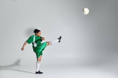 Yeşil futbol forması giyen bir kadın stüdyo ortamında futbol topunu tekmeliyor..
