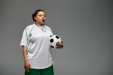 Ağzında düdükle top tutan bir kadın futbol hakemi oyuna başlamaya hazır..