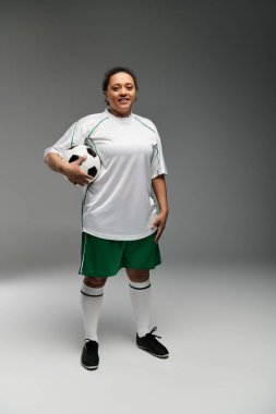 Beyaz formalı ve yeşil şortlu bayan sporcu, futbol topuyla harekete geçmeye hazır..