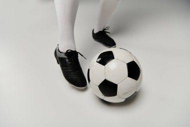 A woman in soccer cleats stands in a studio with a ball at her feet. clipart