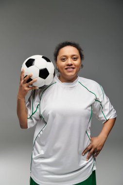 Beyaz formalı bir kadın futbol topu tutuyor ve kameraya gülümsüyor..